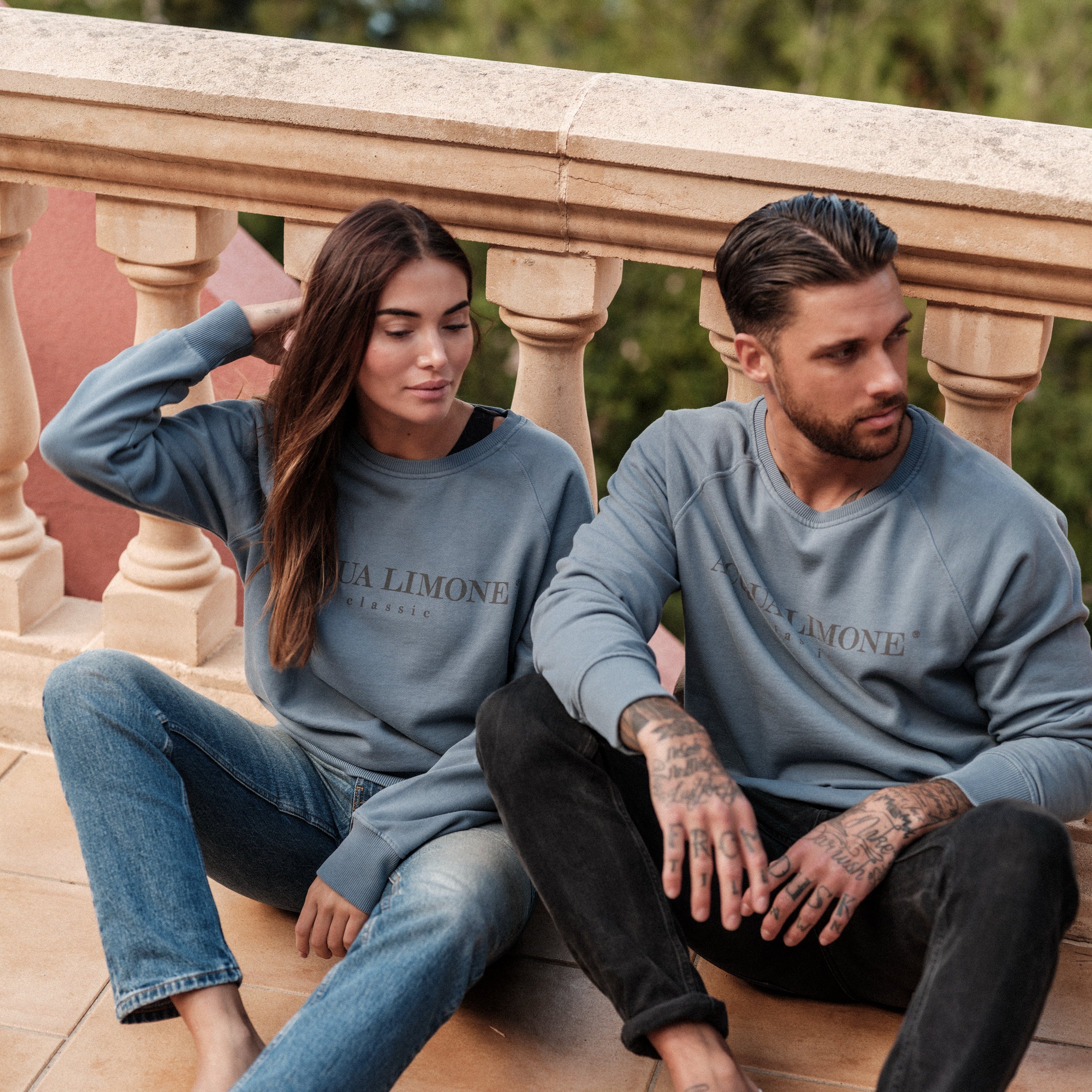 Two people sitting on a balcony wearing matching blue sweatshirts with 'Acqua Limone' branding.