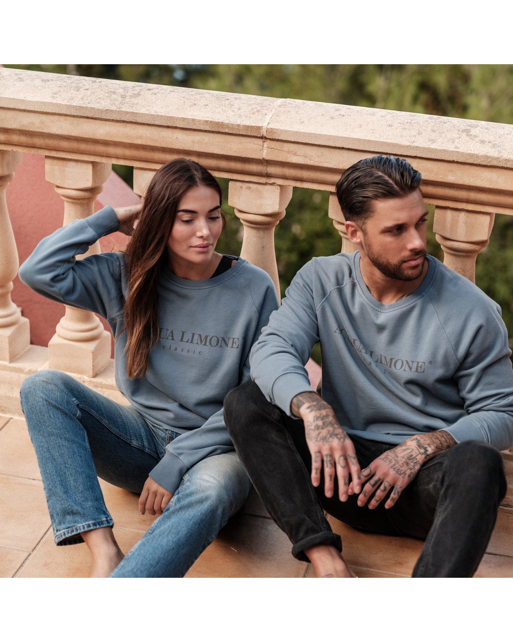 Two people sitting on a balcony wearing matching blue sweatshirts with 'Acqua Limone' branding.