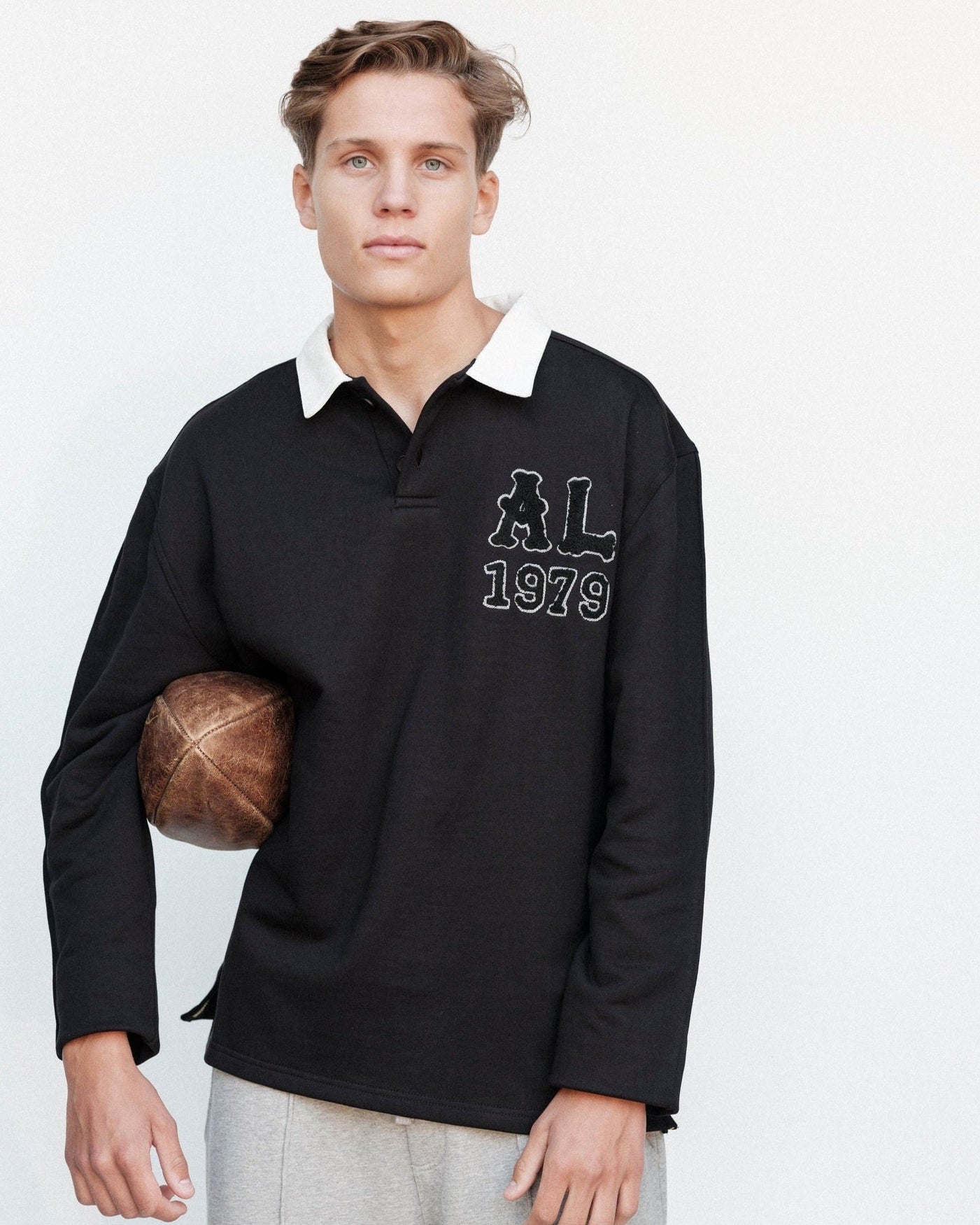 Man wearing a black long-sleeve shirt with a logo and text, holding a basketball on a white background