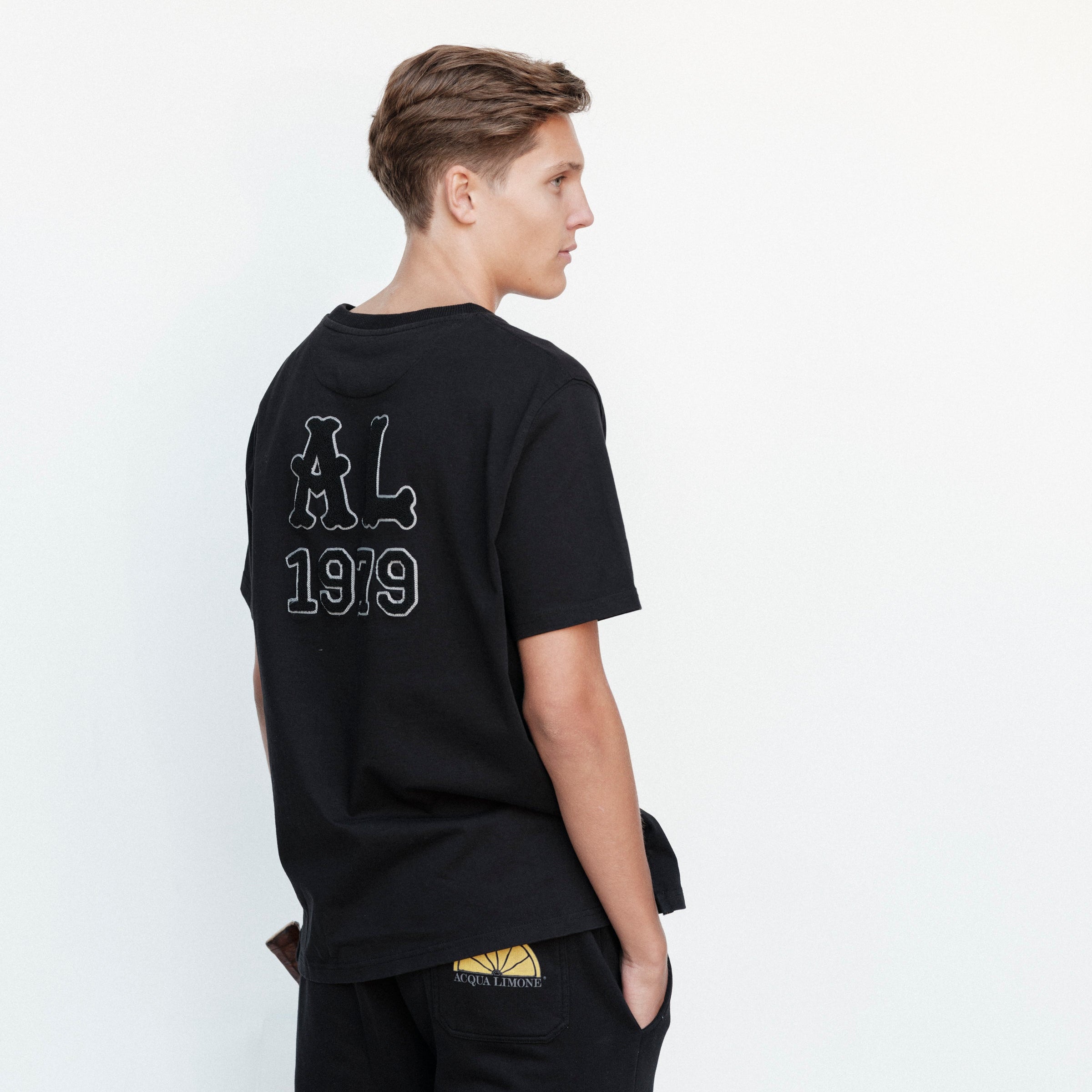 Person wearing a black t-shirt with 'AL 1919' text on the back, standing against a white background.