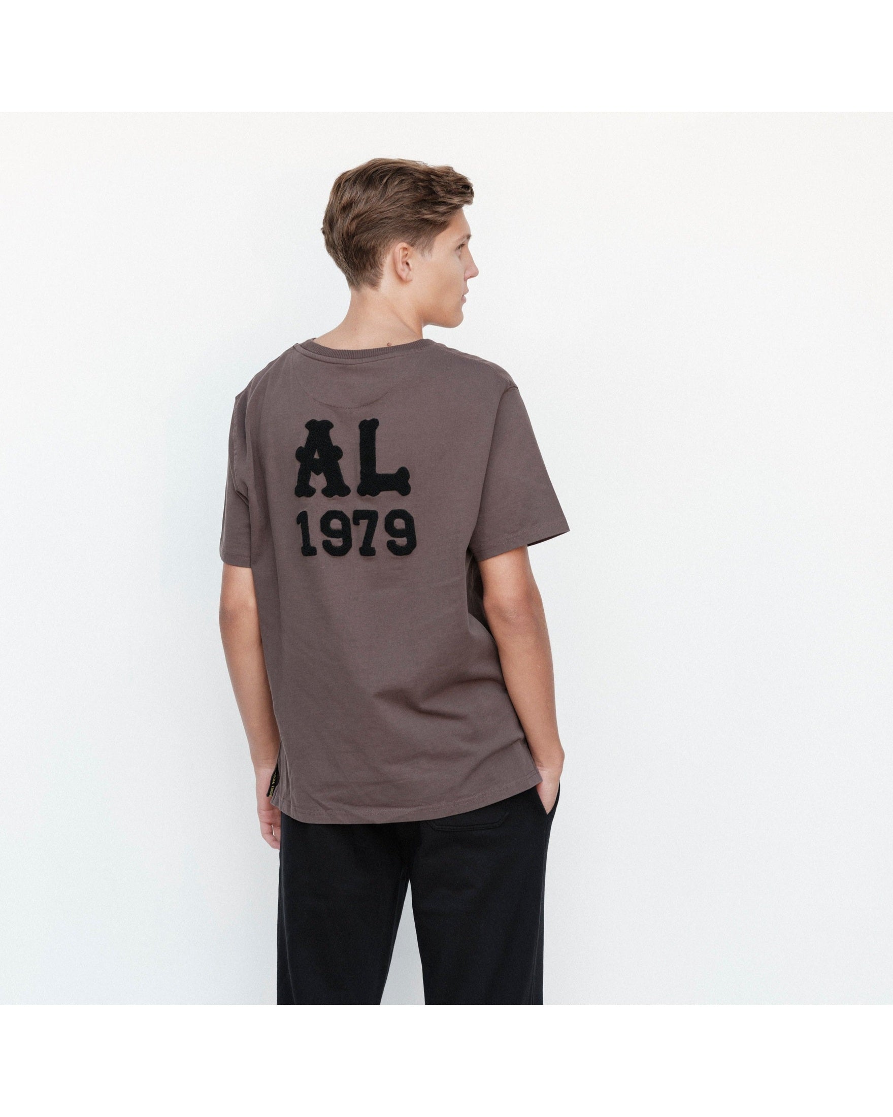 Person wearing a brown t-shirt with 'AL 1979' on the back against a white background