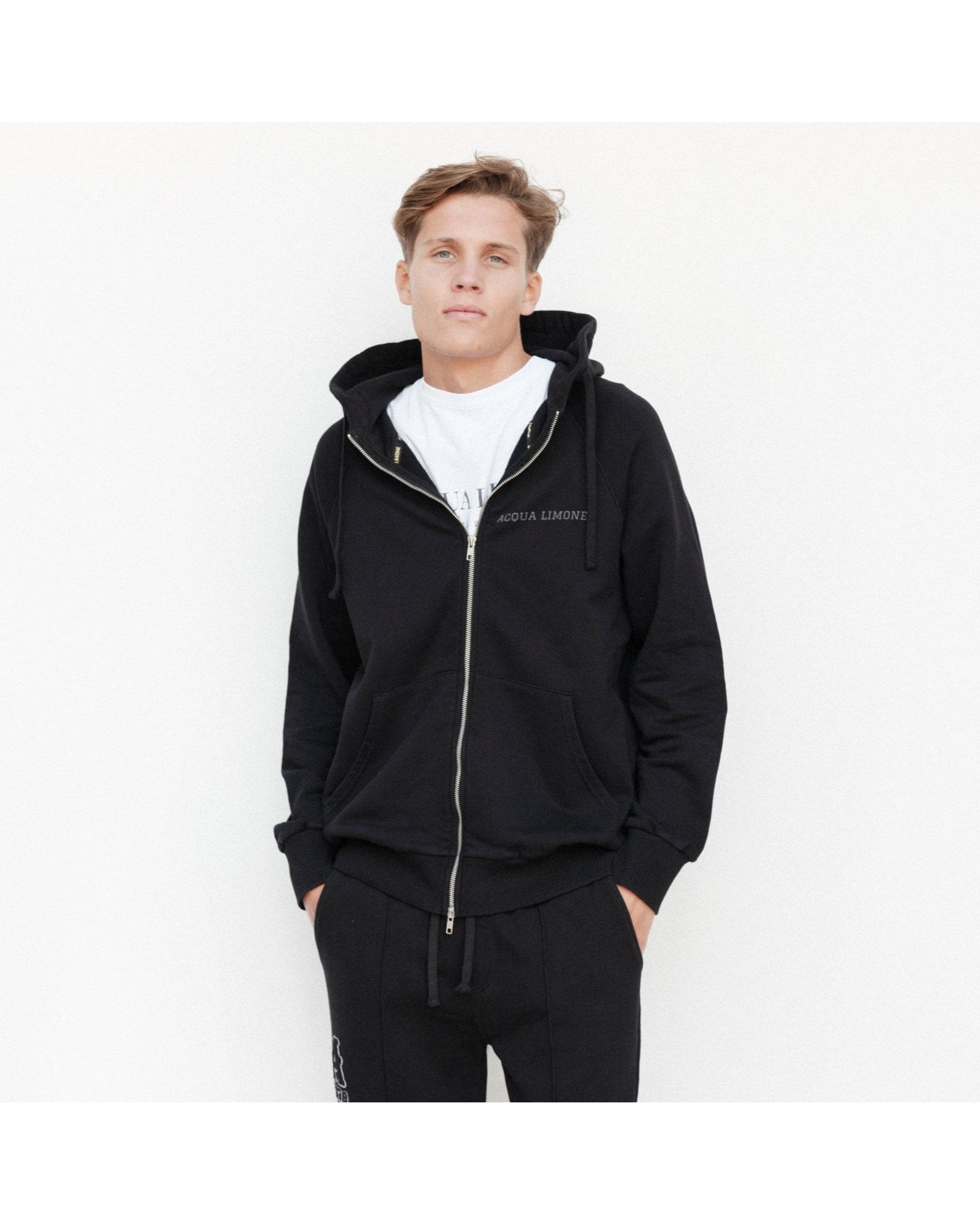Person wearing a black tracksuit with a white logo on a white background