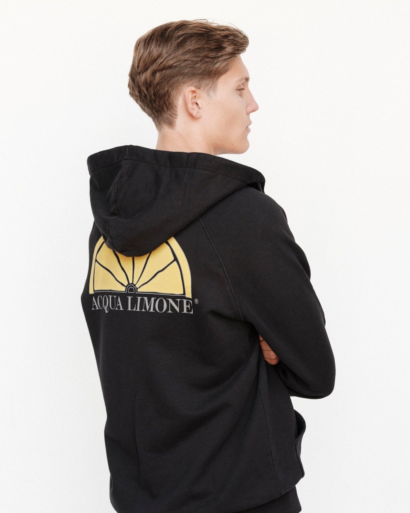 Person wearing a black hoodie with a yellow logo on the back, standing against a white background