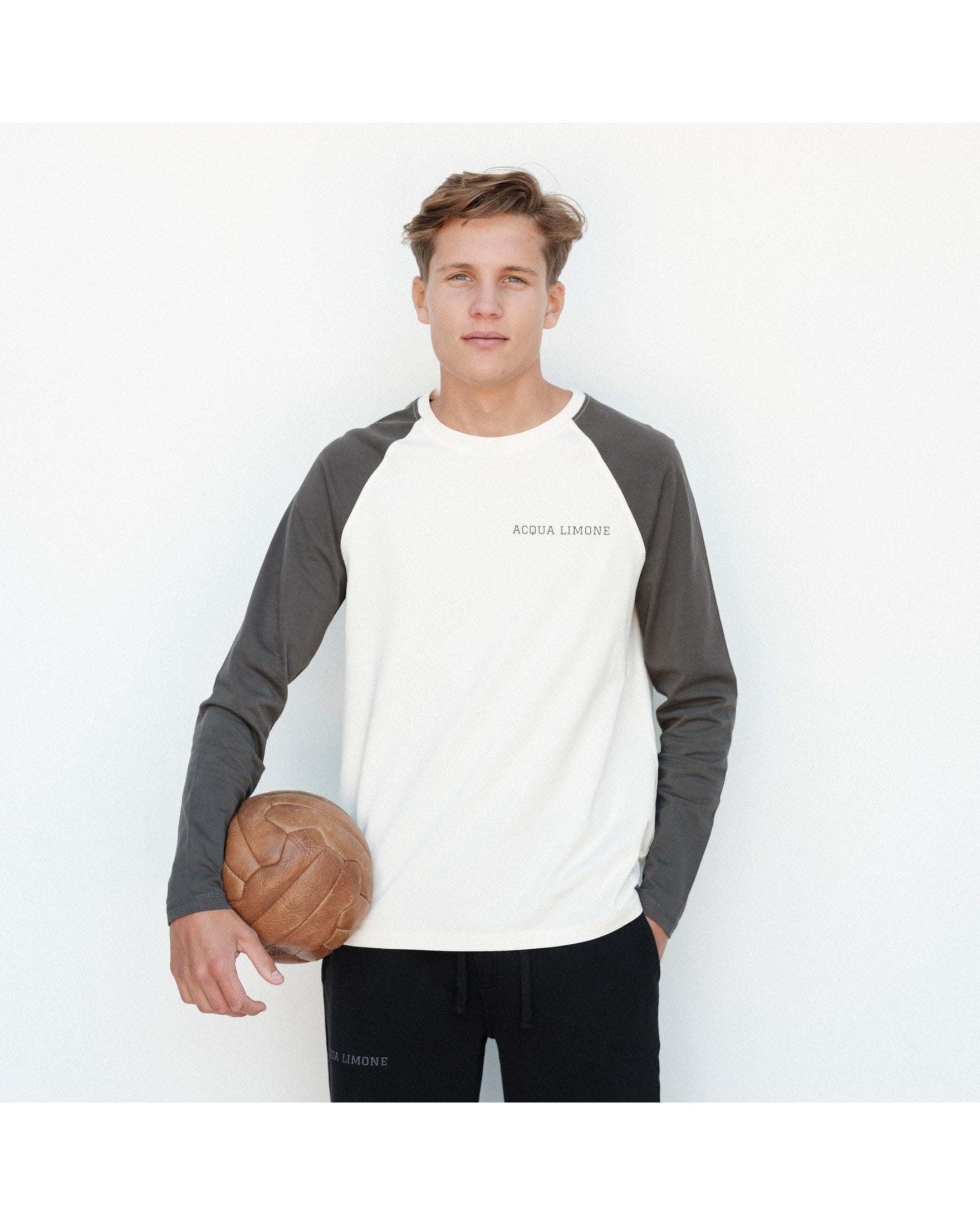 Person wearing a gray and white baseball shirt holding a basketball on a white background