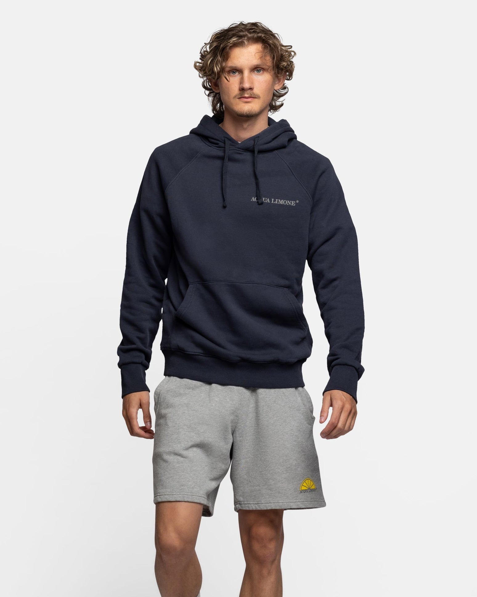Man wearing a navy hoodie and gray shorts on a white background
