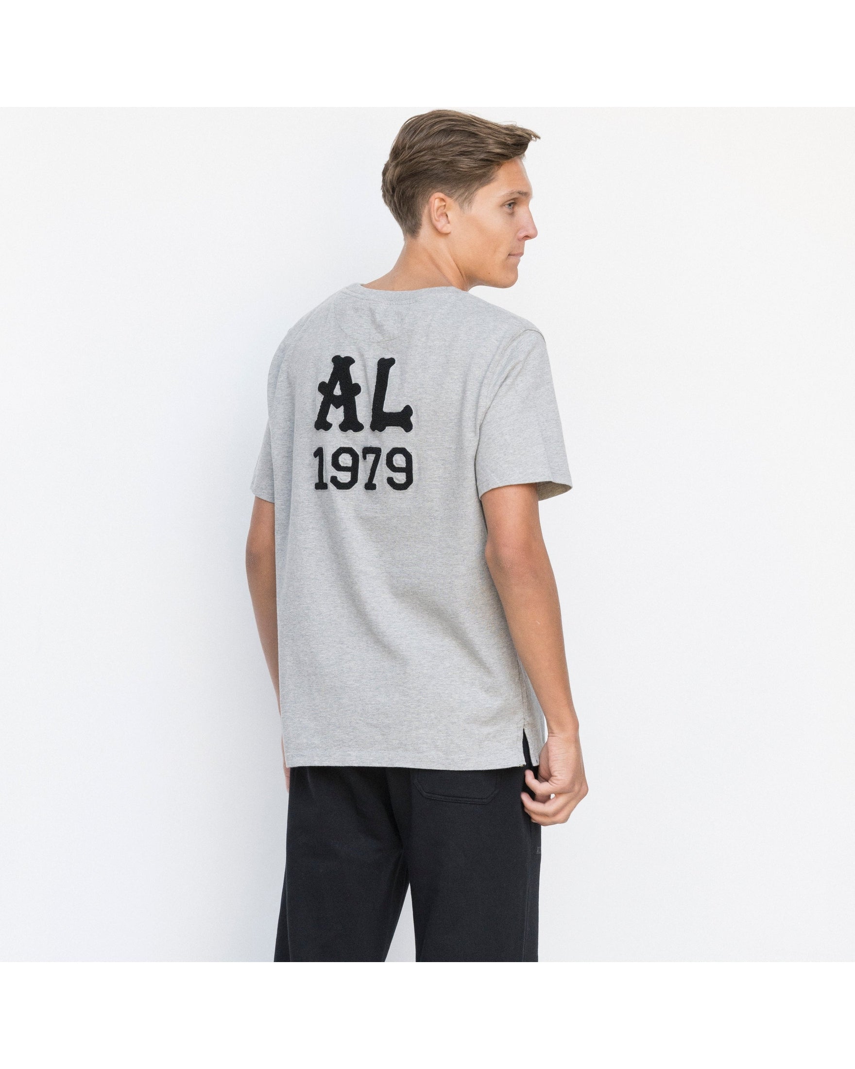Person wearing a gray t-shirt with 'AL 1979' text on the back, standing against a white background.