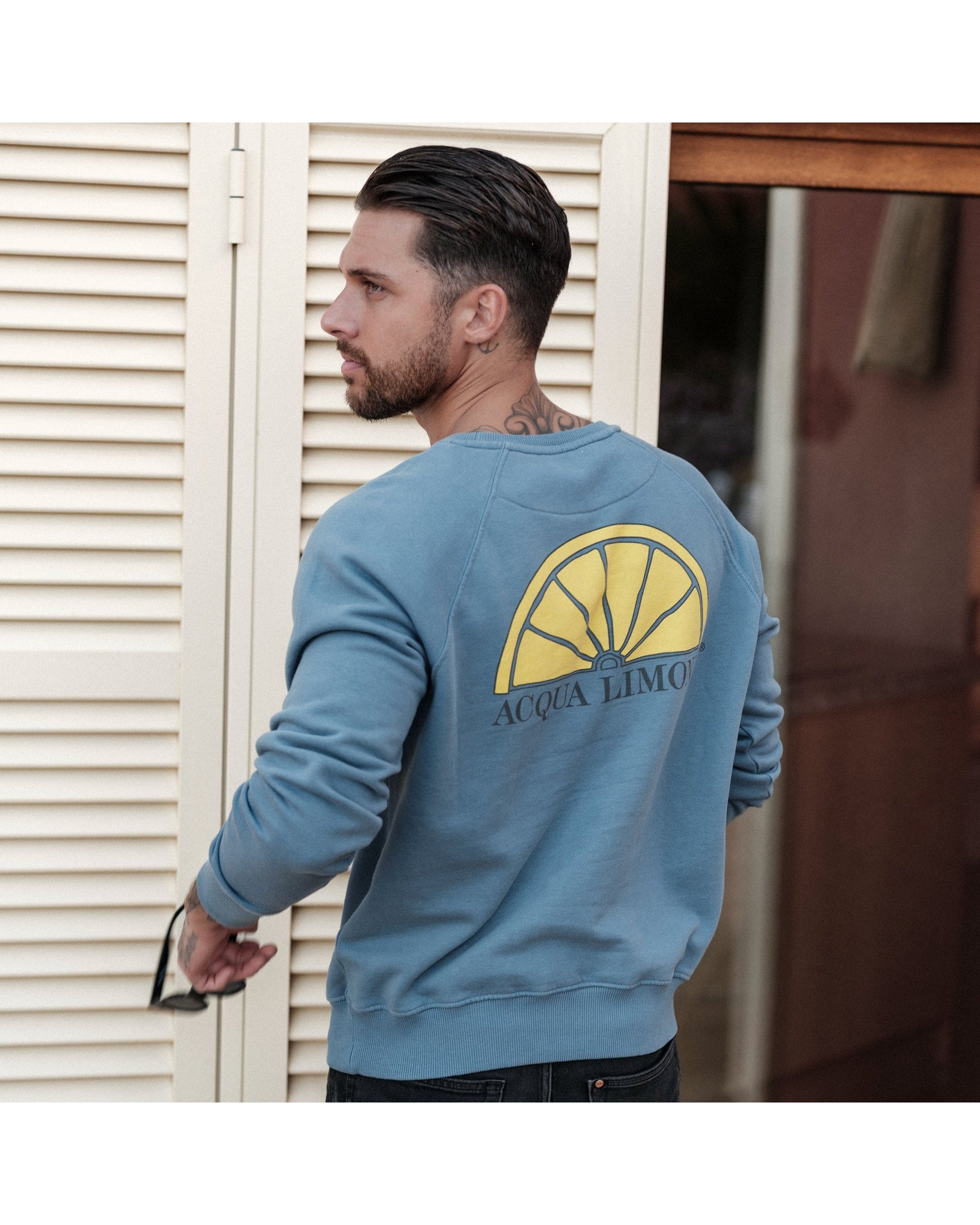 Man wearing a blue sweatshirt with a yellow logo and text, standing in front of a white shutter.
