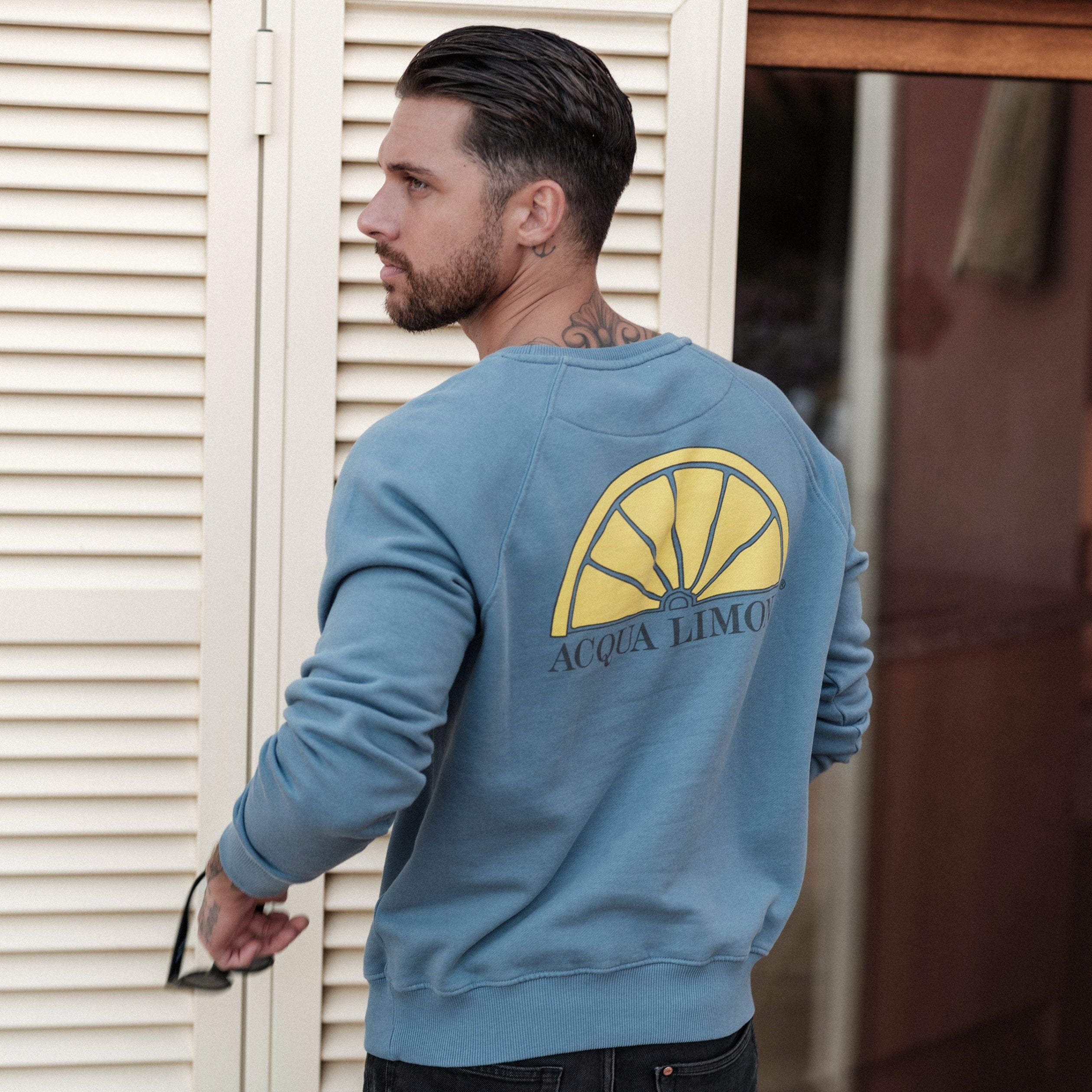 Man wearing a blue sweatshirt with a yellow logo and text, standing in front of a white shutter.