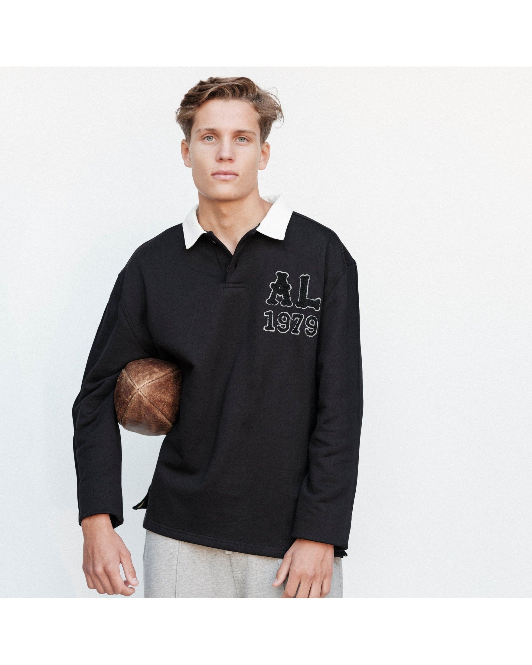 Man wearing a black long-sleeve shirt with a logo and text, holding a basketball on a white background