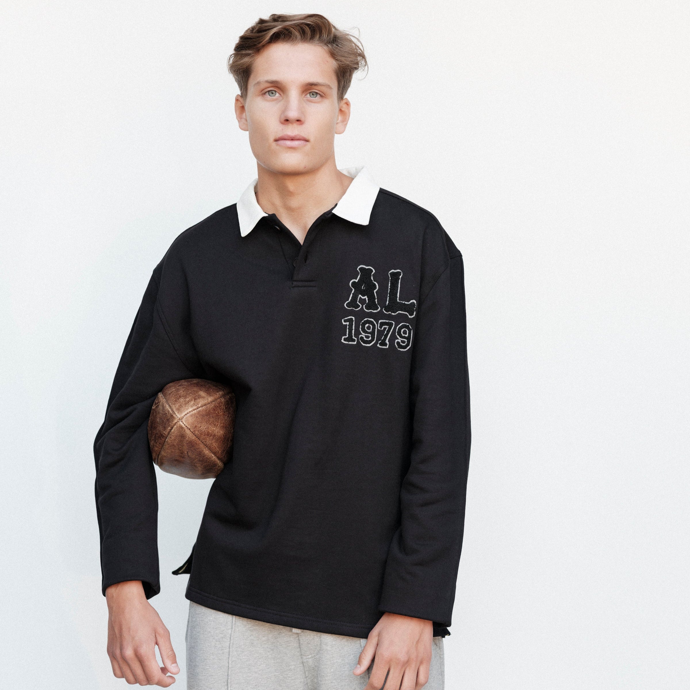 Man wearing a black long-sleeve shirt with a logo and text, holding a basketball on a white background