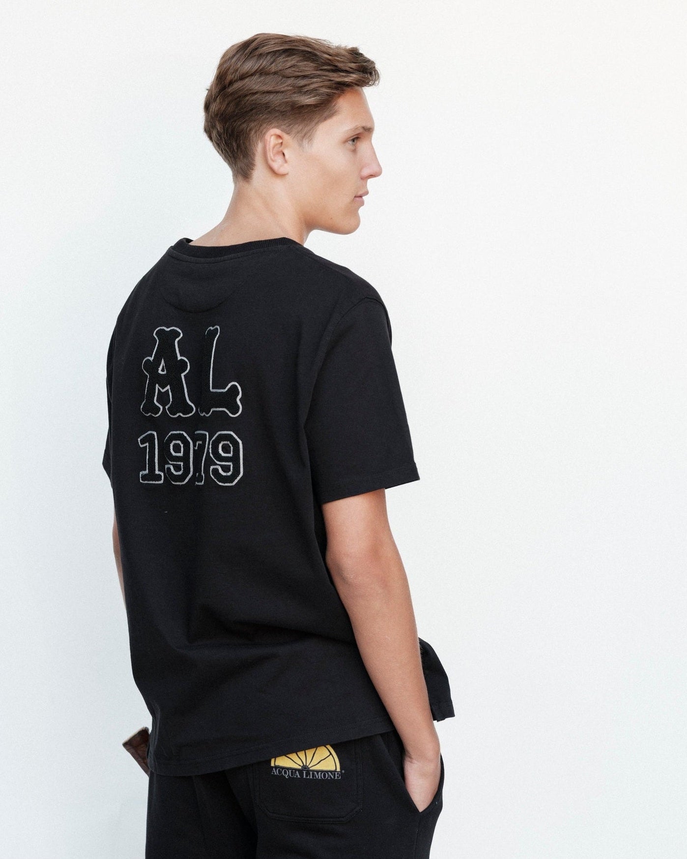 Person wearing a black t-shirt with 'AL 1919' text on the back, standing against a white background.