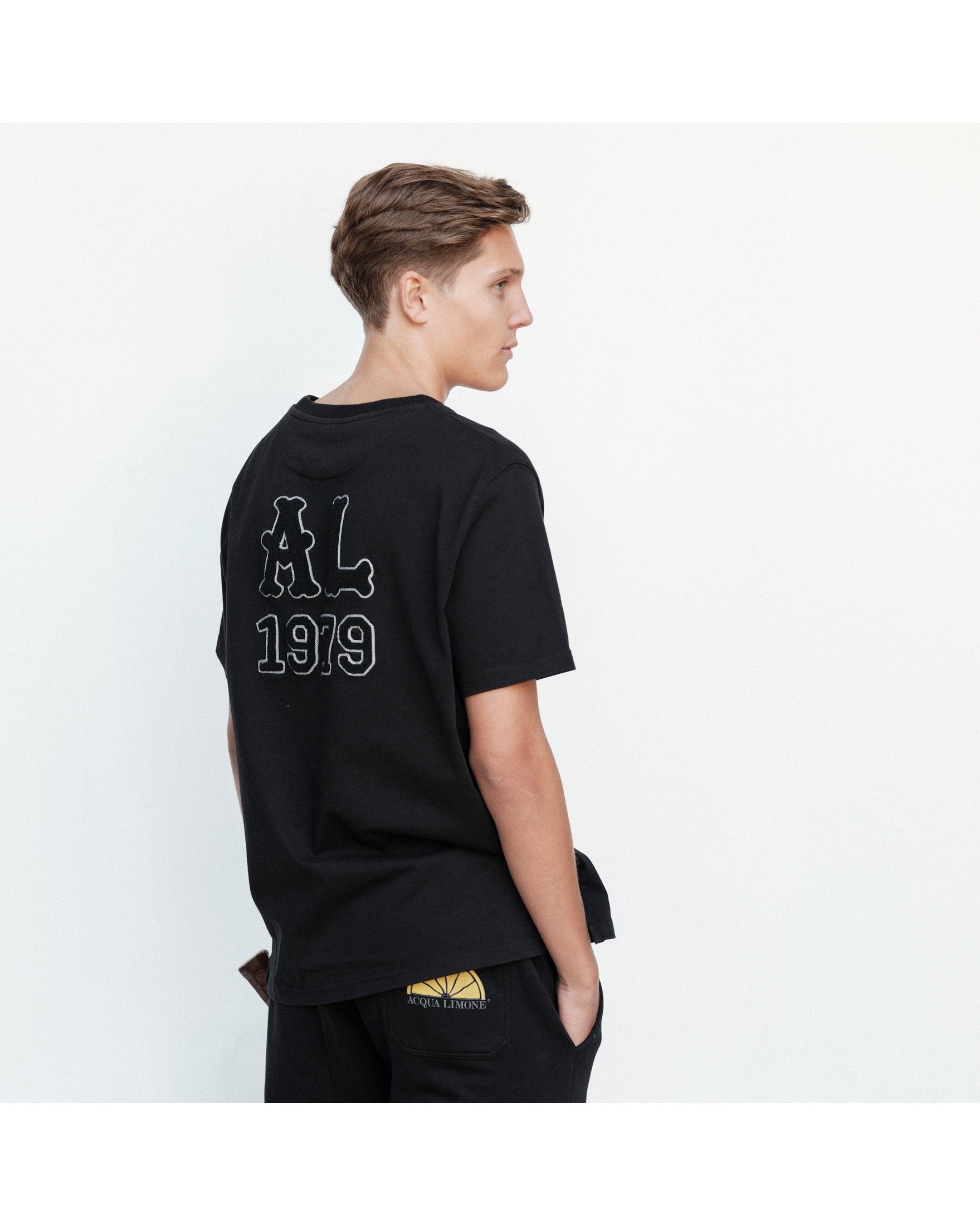 Person wearing a black t-shirt with 'AL 1919' text on the back, standing against a white background.