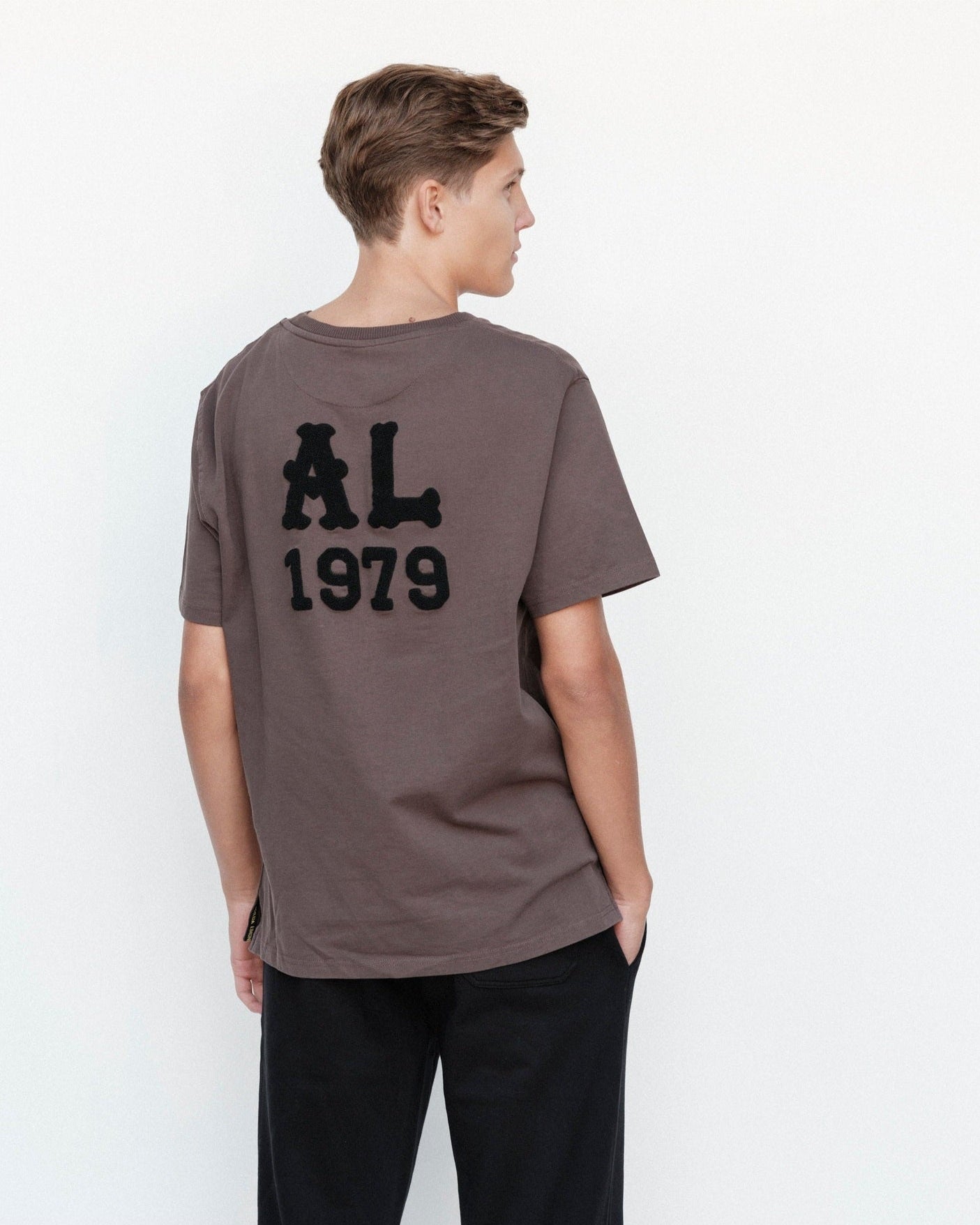 Person wearing a brown t-shirt with 'AL 1979' on the back against a white background