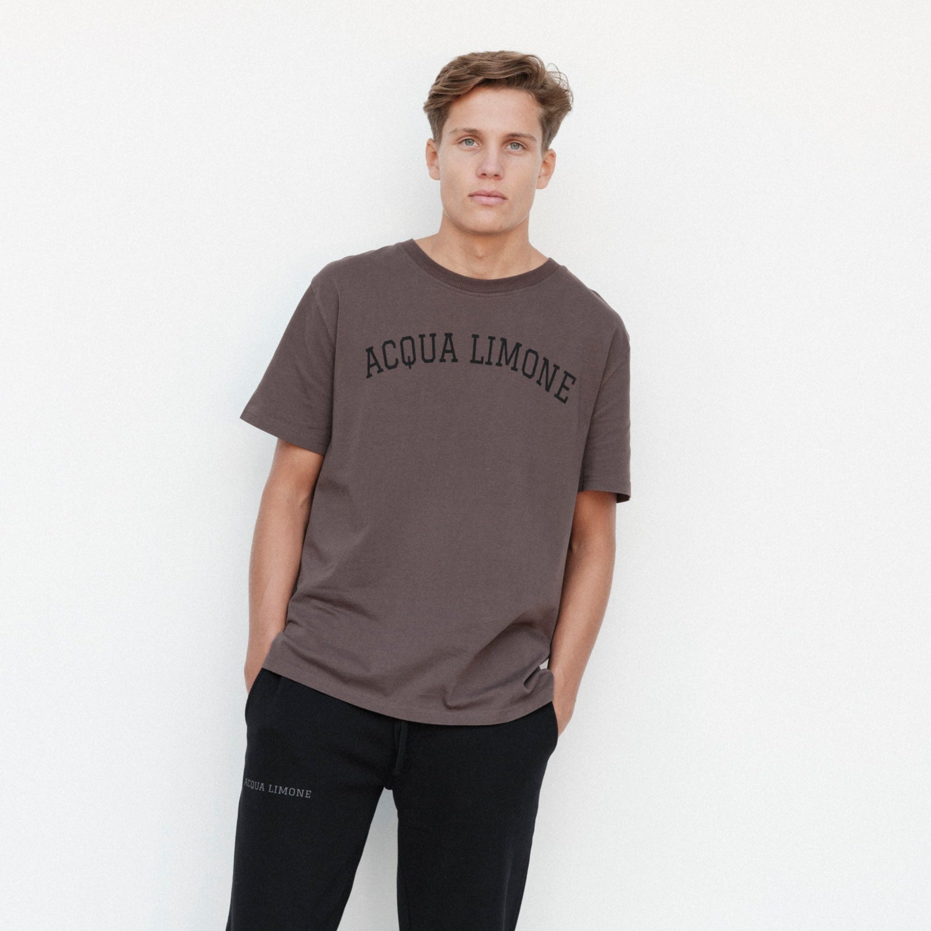 Man wearing a brown 'Acqua Limone' t-shirt against a white background
