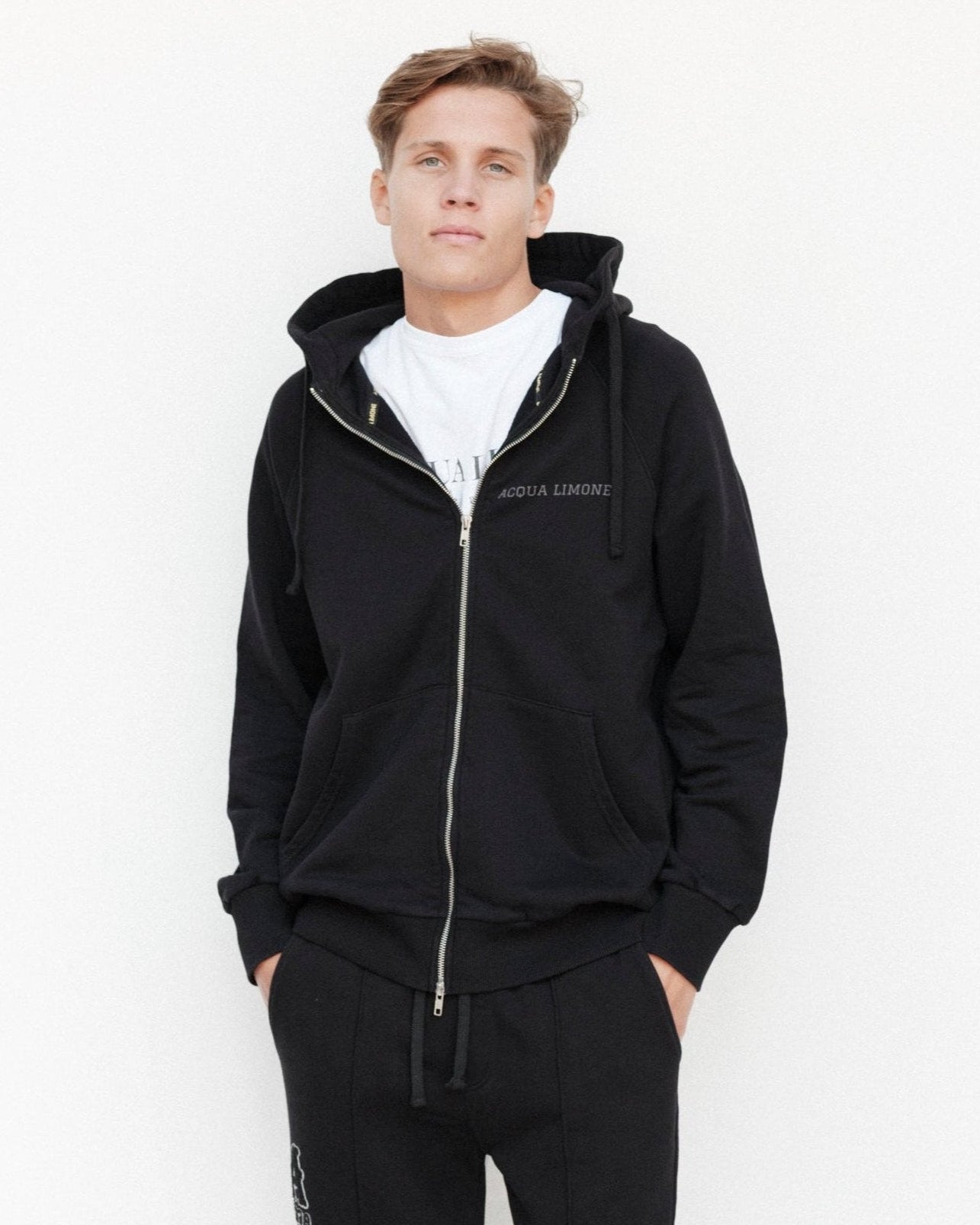 Person wearing a black tracksuit with a white logo on a white background
