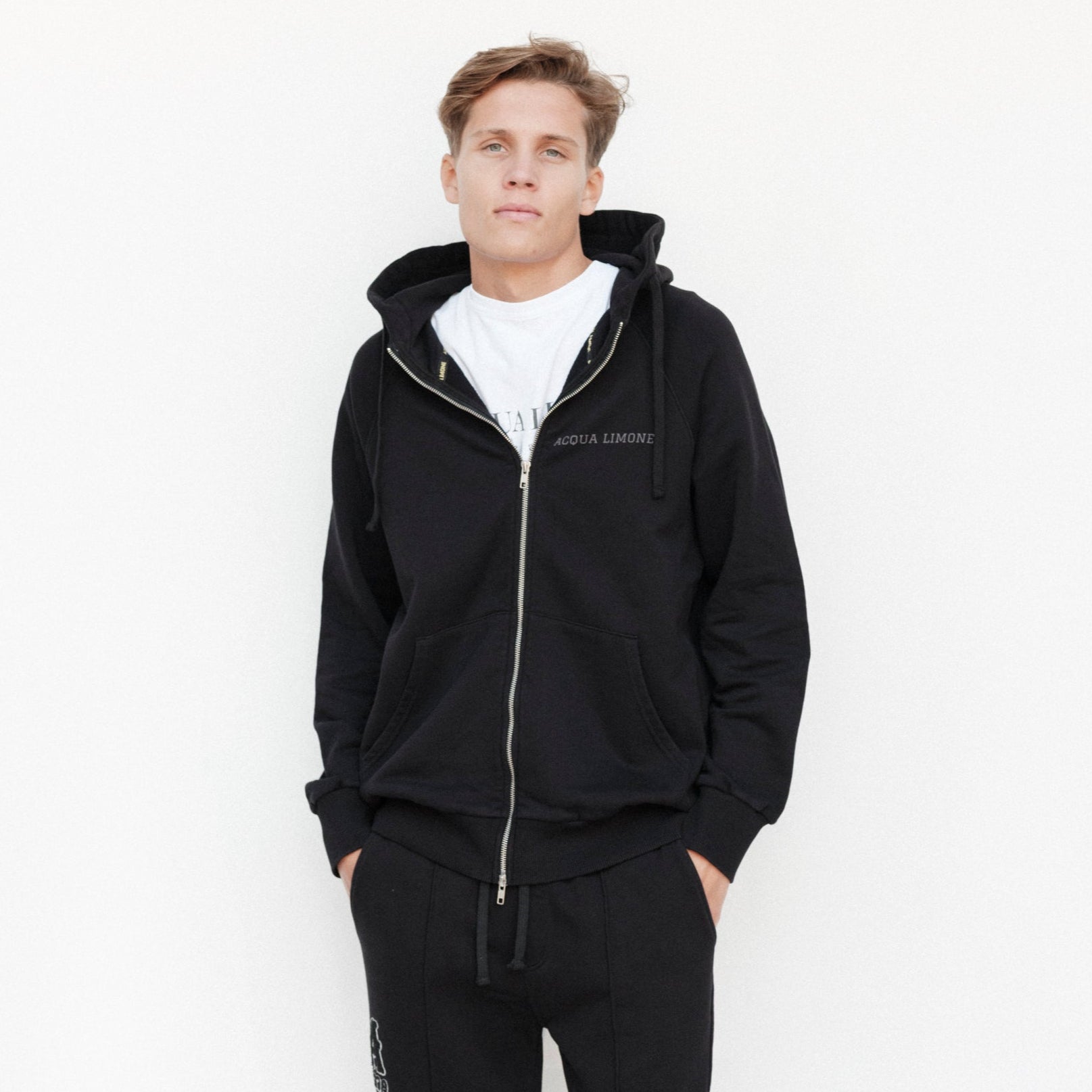 Person wearing a black tracksuit with a white logo on a white background