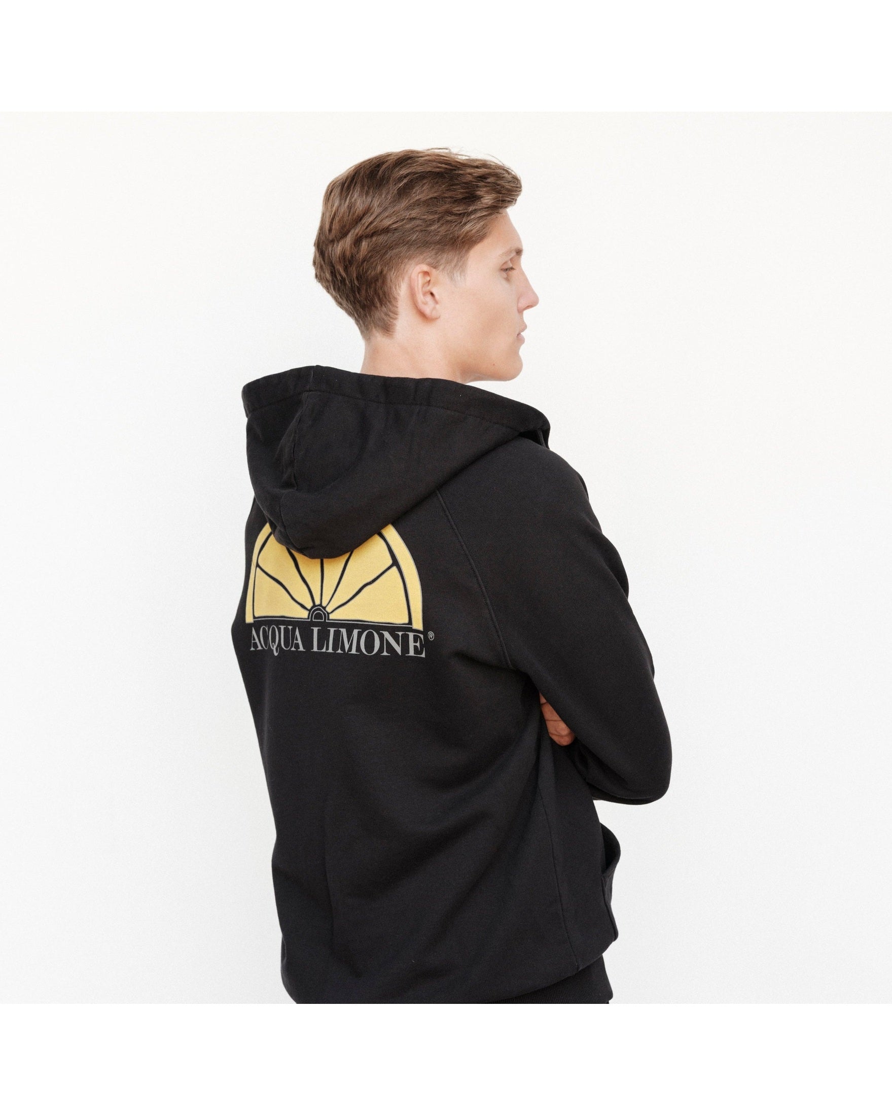 Person wearing a black hoodie with a yellow logo on the back, standing against a white background