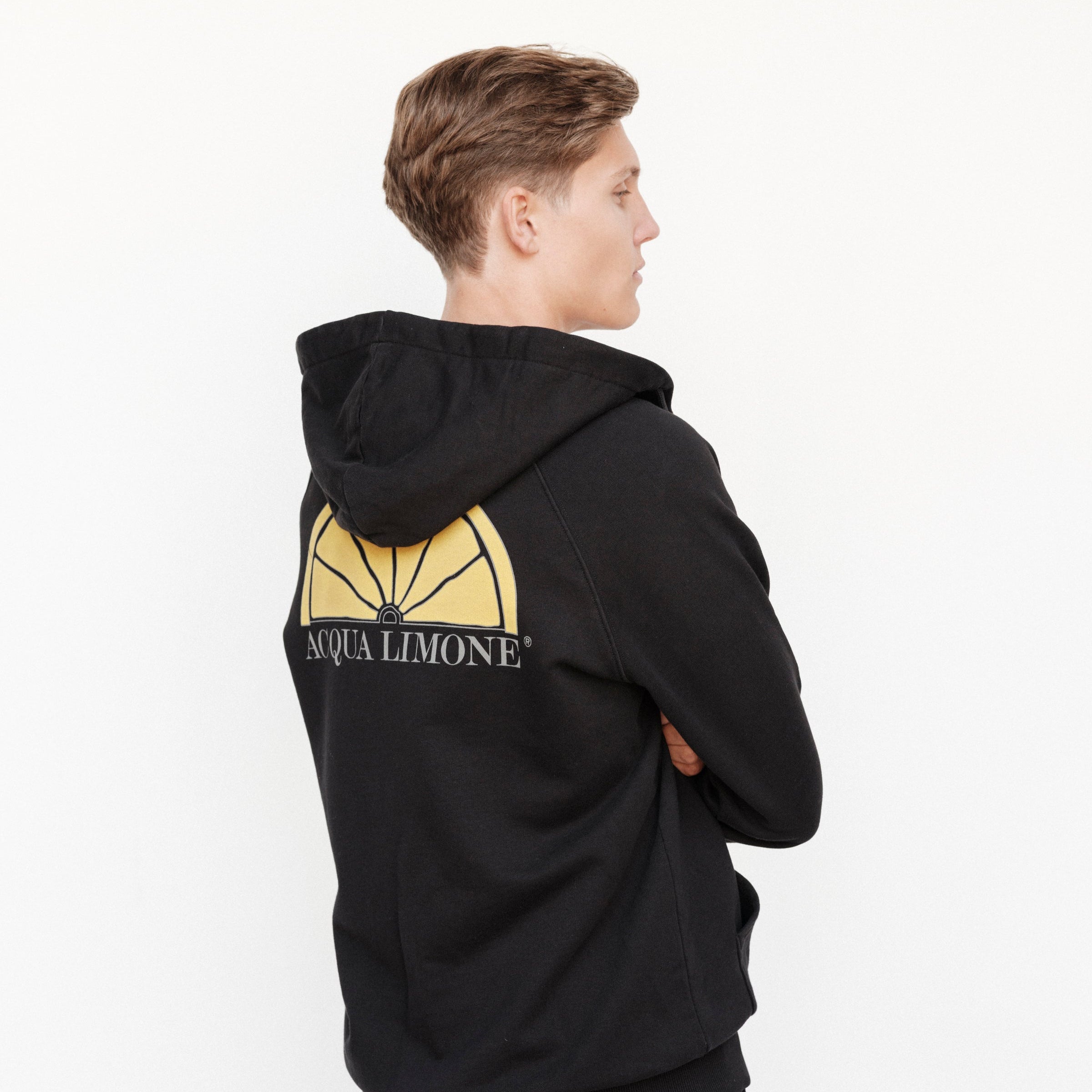 Person wearing a black hoodie with a yellow logo on the back, standing against a white background