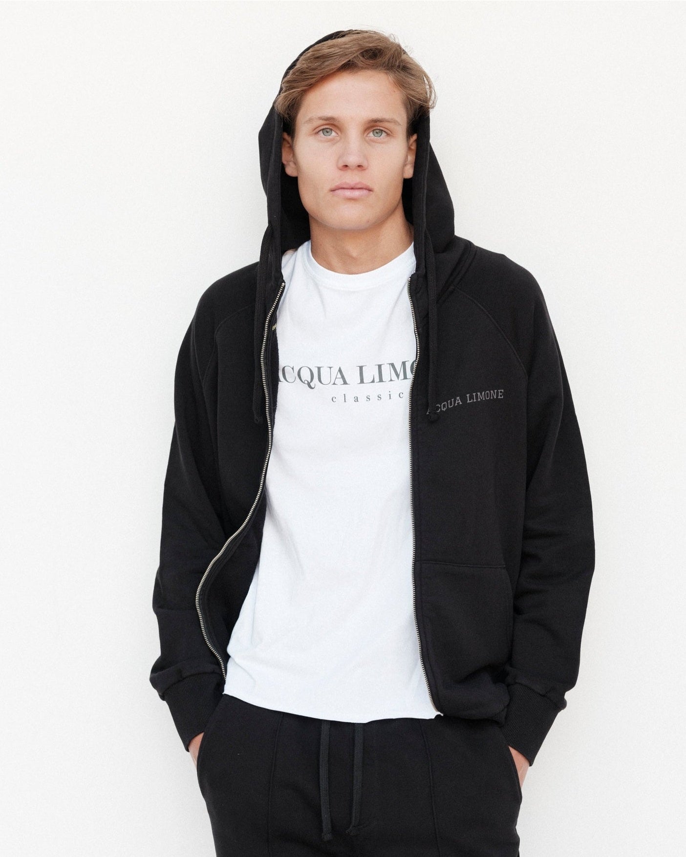 Person wearing a black hoodie and white t-shirt with 'Acqua Limone' branding on a white background