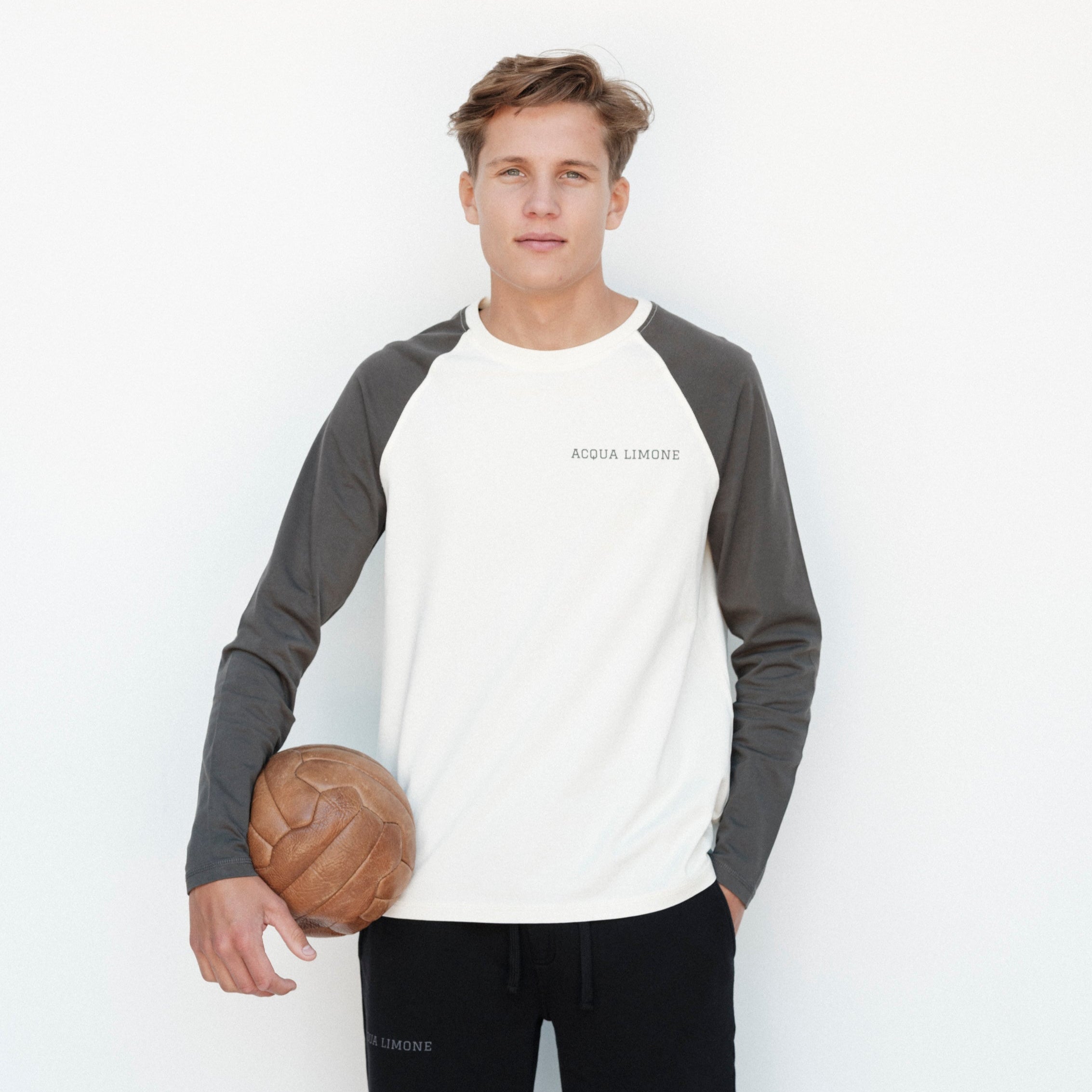 Person wearing a gray and white baseball shirt holding a basketball on a white background