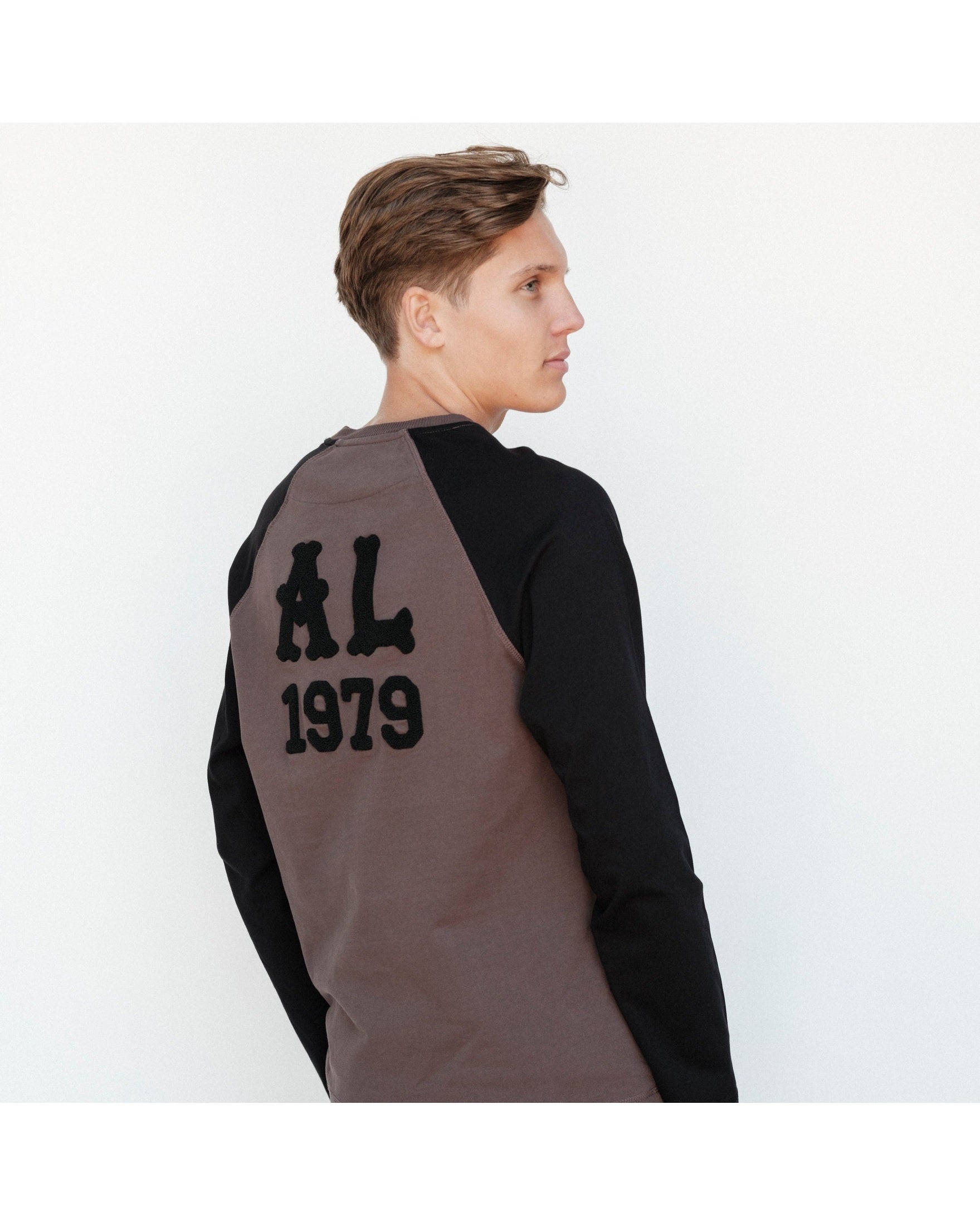 Person wearing a black and gray long-sleeve shirt with 'AL 1979' text on the back against a white background