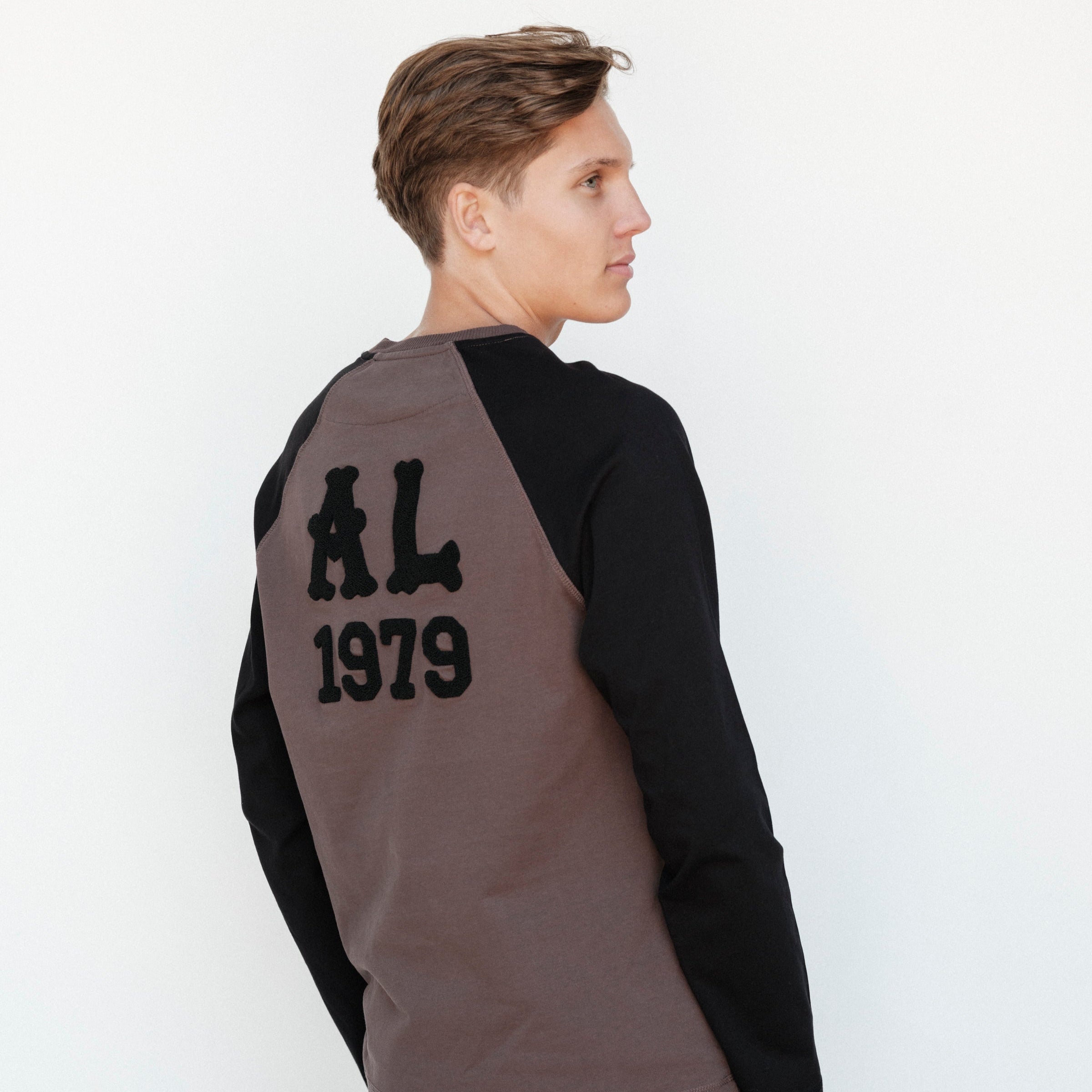 Person wearing a black and gray long-sleeve shirt with 'AL 1979' text on the back against a white background