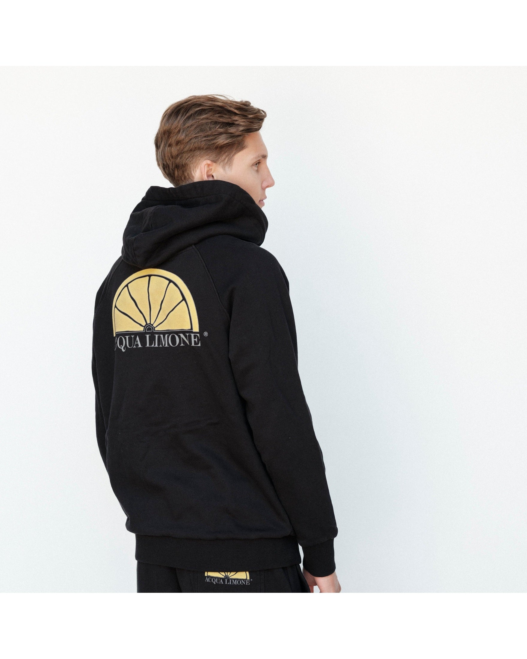 Person wearing a black hoodie with a logo on the back against a white background