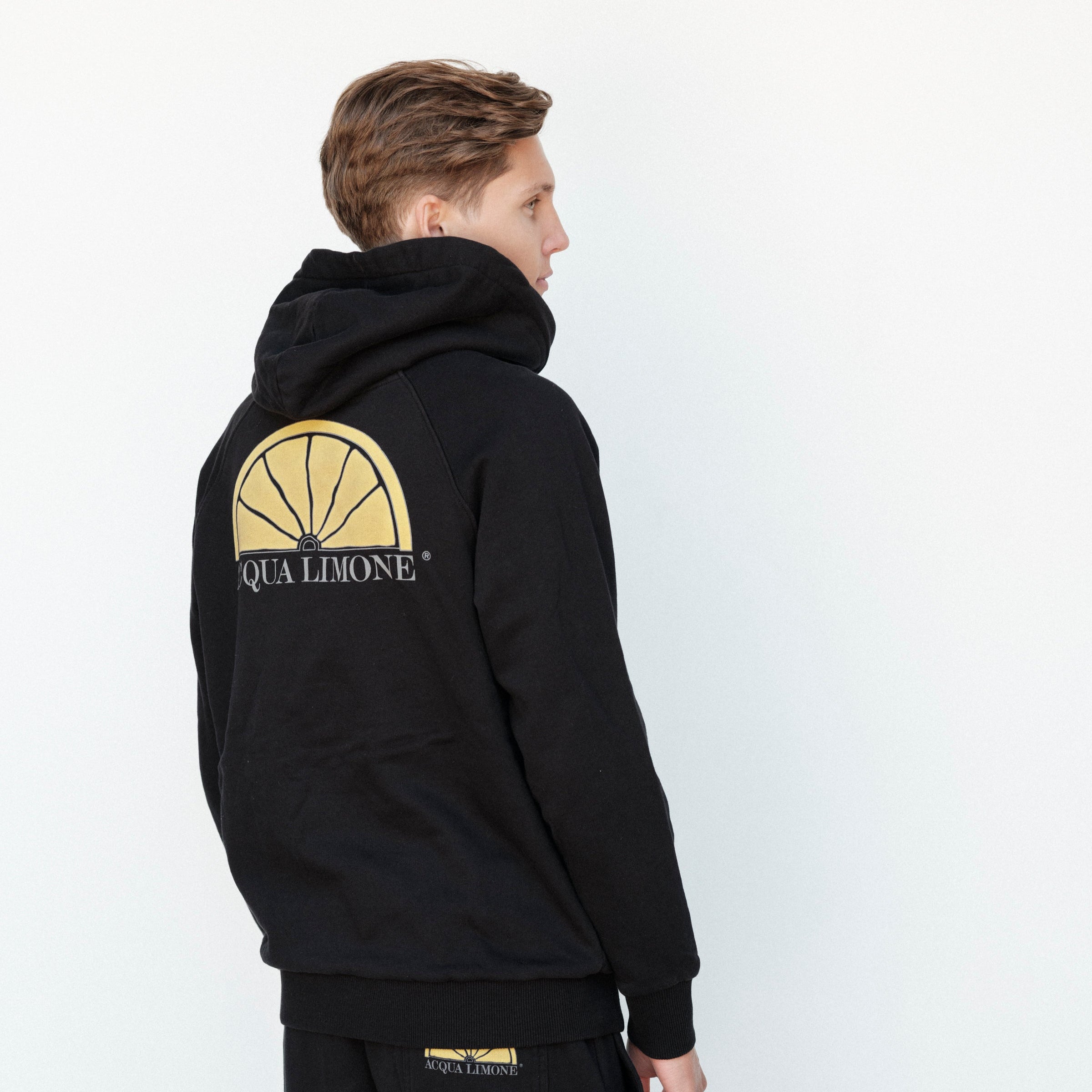 Person wearing a black hoodie with a logo on the back against a white background
