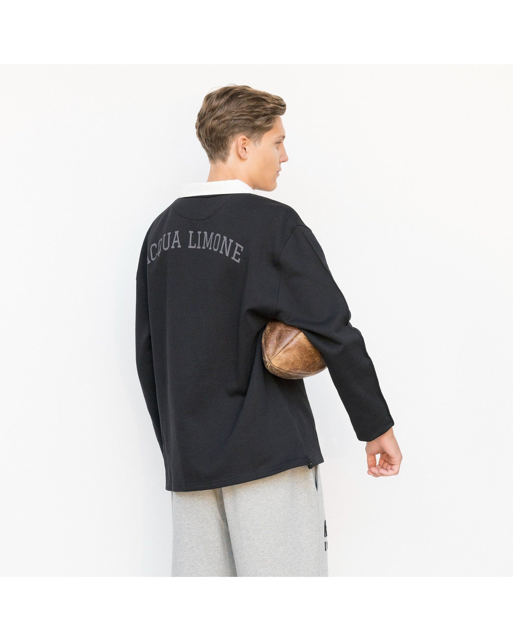 Person wearing a black sweater with 'Acqua Limone' text, holding a football, on a white background