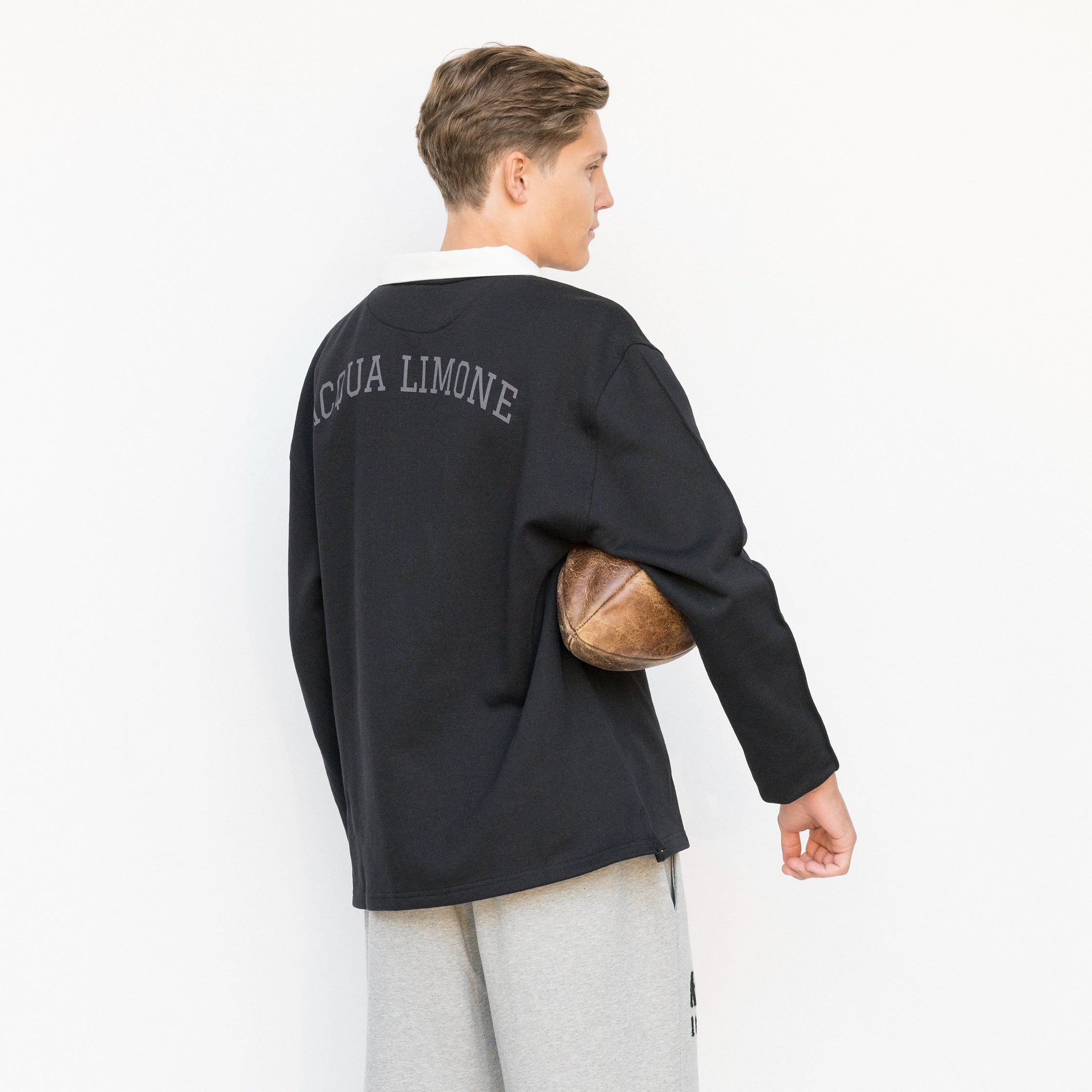 Person wearing a black sweater with 'Acqua Limone' text, holding a football, on a white background